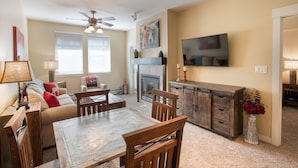 A living room with a fireplace, a dining table, and a TV mounted on the wall. - Fraser Crossing/Founders Pointe, Condo | Gondola Access (Premium-Rated Condo 3624) (Winter Park)