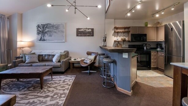 A modern living room with a sofa, coffee table, and a dining area. It includes a kitchen with a refrigerator, microwave, and bar counter. - Zephyr Mountain Lodge, Condo | Ski Storage (Select-Rated Condo 2700) (Winter Park)