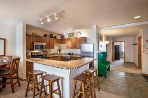 Een moderne keuken met granieten aanrechtbladen, houten kastjes, een centraal eiland met krukken, roestvrijstalen apparatuur en een groene stoel.