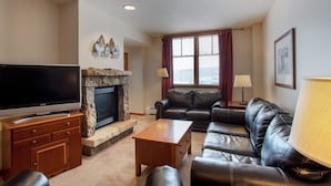 A living room with a television, leather sofa, fireplace, and a large window with curtains. - Zephyr Mountain Lodge, Condo | Balcony Slopes View (Select-Rated Condo 1620) (Winter Park)