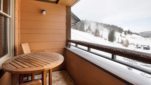 A balcony with a wooden table and chair, overlooking a snowy landscape with trees and a ski lift. - Zephyr Mountain Lodge, Condo | Balcony Slopes View (Select-Rated Condo 1620) (Winter Park)