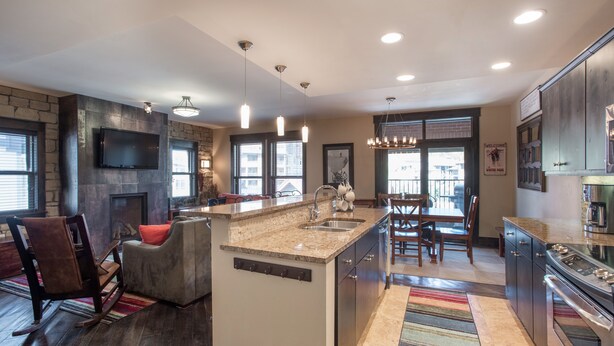 A modern kitchen with a large island, built-in appliances, and a dining area with a chandelier. - Village View, Townhouse | Fireplace at Parry Peak Lofts (Premium-Rated Condo 106) (Winter Park)