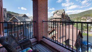 A balcony with wicker chairs and a view of a town with buildings and a mountain in the background. - Village View, Townhouse | Fireplace at Parry Peak Lofts (Premium-Rated Condo 106) (Winter Park)