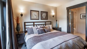 A bedroom with a large bed, dark wood headboard, two wall-mounted lamps, and a framed artwork on the wall. - Village View, Townhouse | Fireplace at Parry Peak Lofts (Premium-Rated Condo 106) (Winter Park)