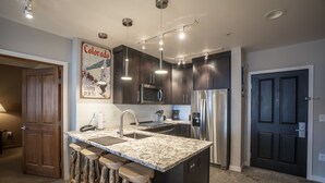 Una cocina moderna con armarios oscuros, electrodomésticos de acero inoxidable, encimera de granito y taburetes de bar.