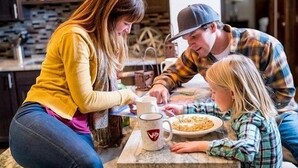 Una familia de tres personas sentada a la mesa del comedor, con un plato de comida y una taza.