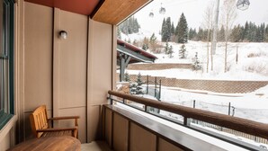 Un balcón con una silla de madera y vistas a un paisaje nevado con un telesilla.
