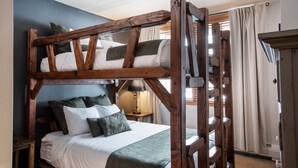 Una cama litera con estructura de madera, ropa de cama blanca y una manta verde.