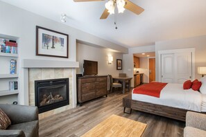 A modern hotel room with a fireplace, a bed with red pillows, a dining area, and a TV. - Fraser Crossing/Founders Pointe, Condo | Top Floor Ski-In/Ski-Out (Premium-Rated Condo 3622) (Winter Park)