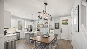 Une cuisine moderne avec des meubles blancs, une table à manger en bois et des luminaires suspendus.