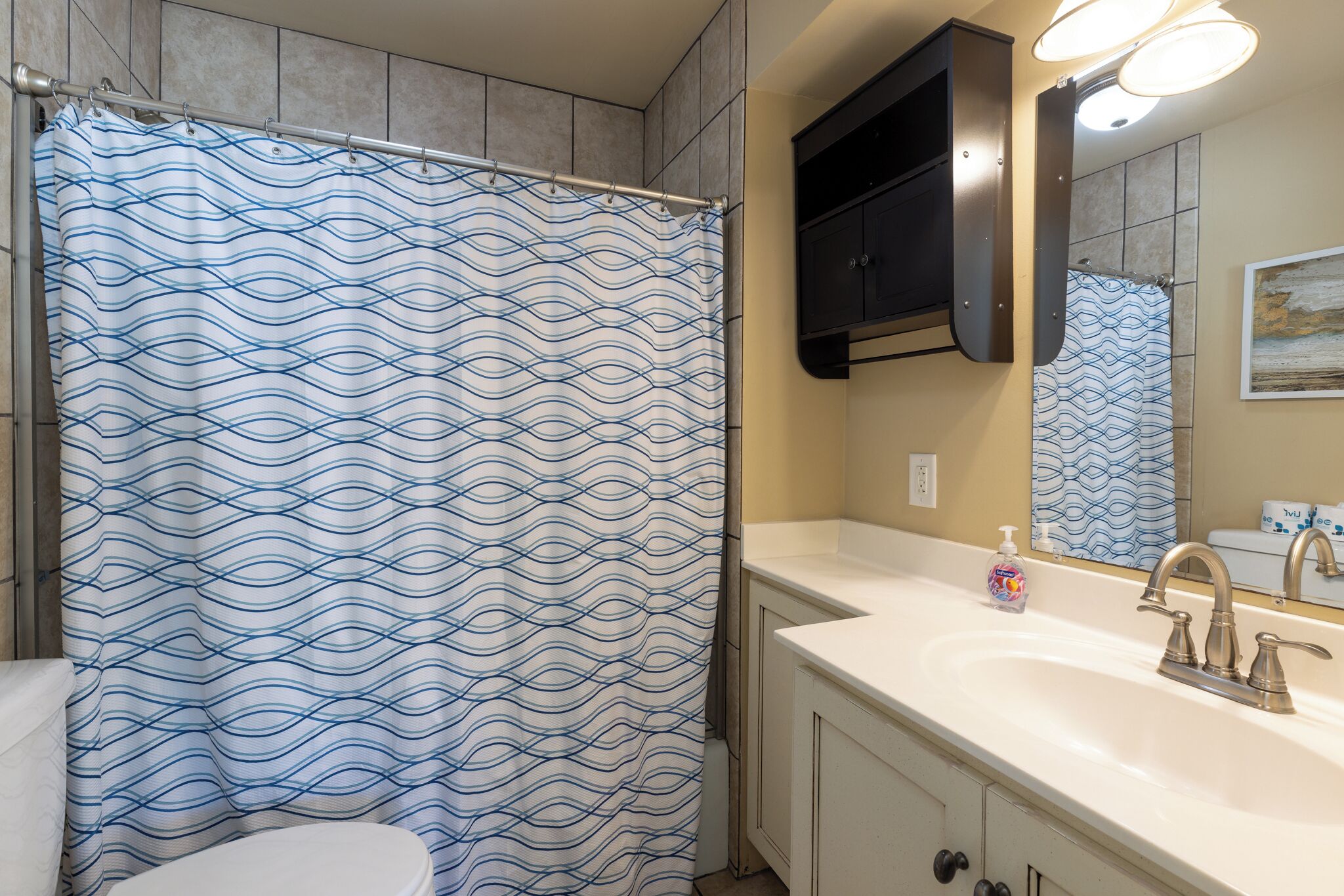 A bathroom with a shower curtain, a sink, a mirror, and a cabinet.