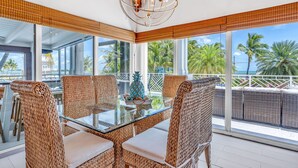 A glass-top dining table with wicker chairs, a decorative pineapple centerpiece, and a view of palm trees and the ocean. - 5BR/4.5BA • Ocean Views • Pool & Hot Tub • Dock • Kayaks • Bikes & More (Key Largo)