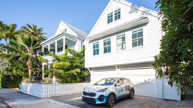 Een wit, twee verdiepingen tellend huis met een garage, een witte picket hek en een Kia Soul die ervoor geparkeerd staat.