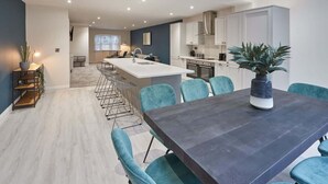 A modern kitchen with white cabinets, a central island, and teal chairs. - Host & Stay | Iburn House (Briggswath)