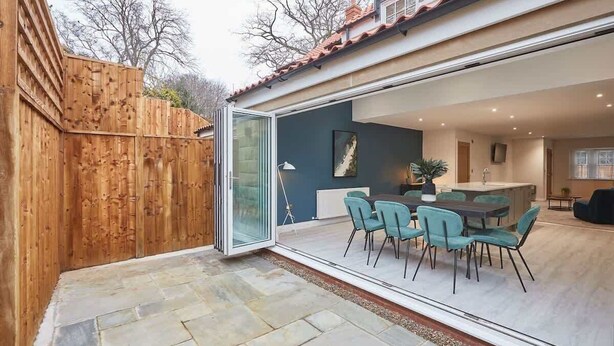 A modern house with a glass door leading to a dining area with teal chairs and a table. - Host & Stay | Iburn House (Briggswath)