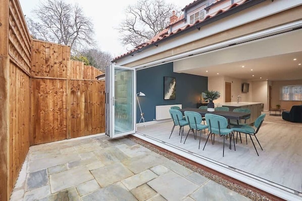 A modern house with a glass door leading to a dining area with teal chairs and a table.