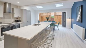 A modern kitchen with a central island, bar stools, and a view of a wooden deck. - Host & Stay | Iburn House (Briggswath)