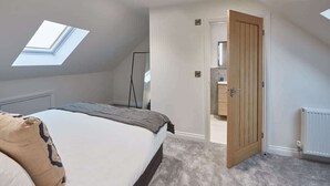 A bedroom with a skylight, a bed, a door leading to a bathroom, and a radiator. - Host & Stay | Iburn House (Briggswath)