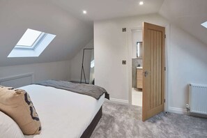 A bedroom with a skylight, a bed, a door leading to a bathroom, and a radiator.