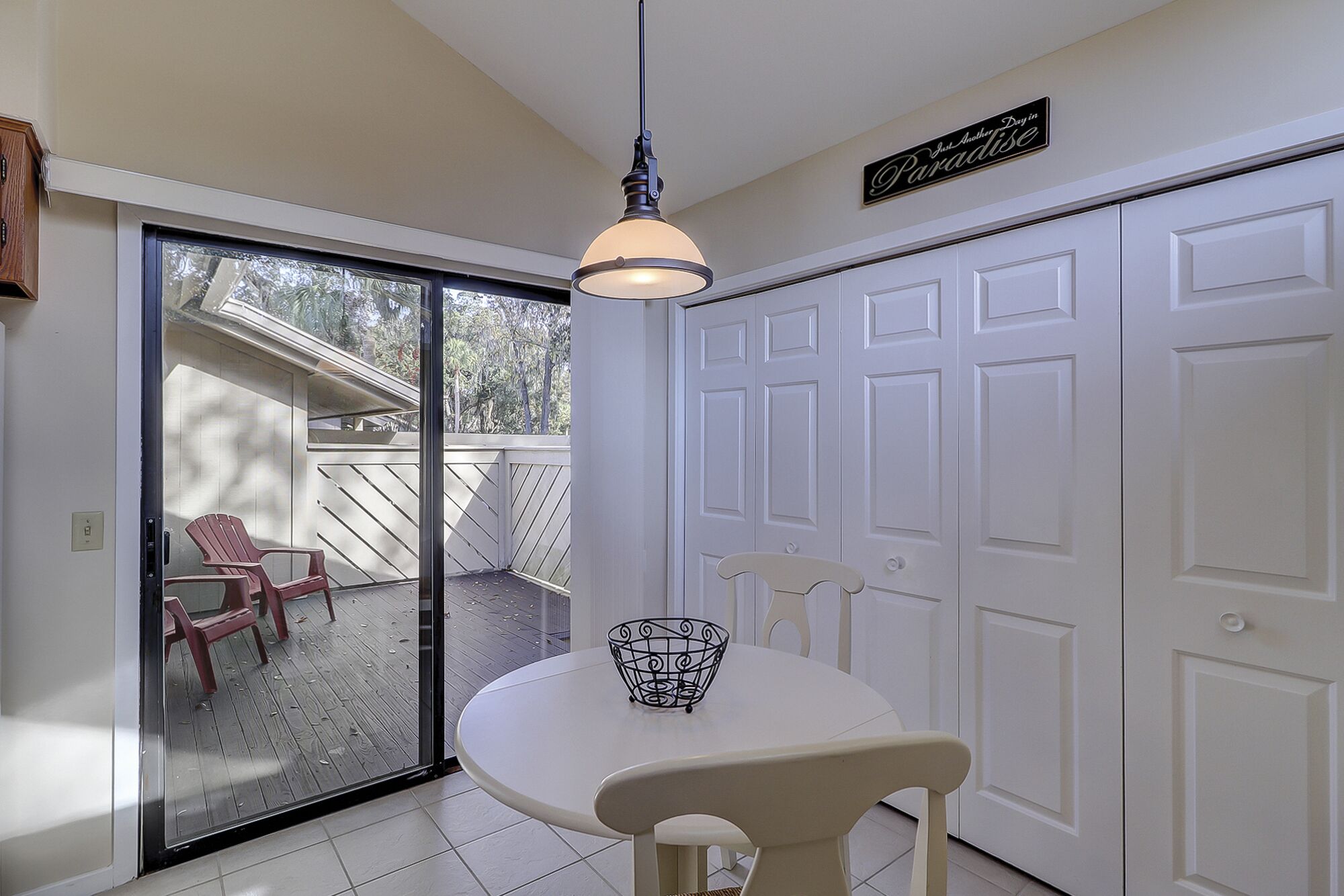 A dining area with a table and chairs, a hanging light fixture, and a sliding glass door leading to an outdoor patio with chairs.