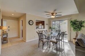 A dining area with a round glass table and six chairs, a ceiling fan, a clock, and a view of the outdoors through a large window. - Sunset Rentals | Ocean Course 556 (Hilton Head Island)