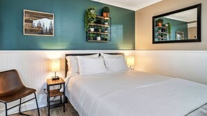 A hotel room with a bed, bedside tables, a chair, a wall-mounted shelf with plants, and a mirror. - Lovely condo w/ indoor pool *only steps to parkway (Gatlinburg)