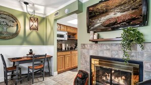 A dining area with a table and chairs, a fireplace with a screen, and a kitchen with wooden cabinets. - Lovely condo w/ indoor pool *only steps to parkway (Gatlinburg)