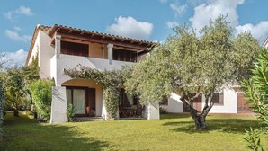 A two-story house with a tiled roof, a covered patio, and a well-maintained lawn.
