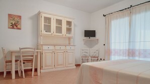 A bedroom with a bed, a TV on a stand, a cabinet, and two chairs.