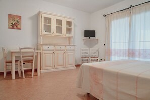 A bedroom with a bed, a TV on a stand, a cabinet, and two chairs.