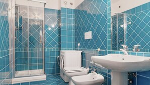 A bathroom with blue tiles, a glass-enclosed shower, a toilet, and a sink.