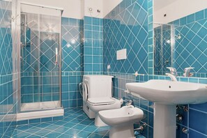 Une salle de bain avec des carreaux bleus, une douche à parois de verre, des toilettes et un lavabo.