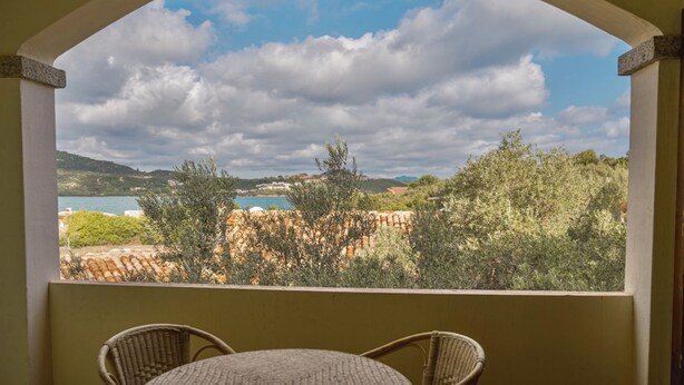 A balcony with a view of a coastal landscape, including trees and a body of water.
