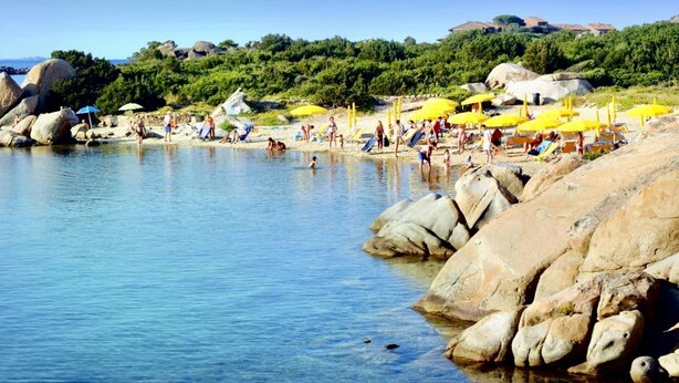 A beach with clear water, rocks, and people.