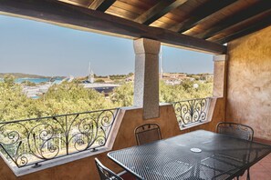 Ein Balkon mit einem Metalltisch und Stühlen, mit Blick auf eine Küstenlandschaft mit Gebäuden und einer Kirche.