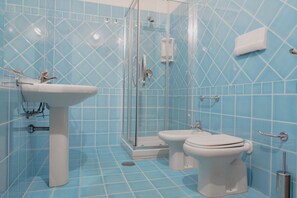 Ein Badezimmer mit Duschkabine aus Glas, Waschbecken und zwei Toiletten.