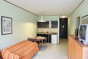 Una habitación compacta con cama, una pequeña mesa de comedor con sillas, kitchenette y televisión.