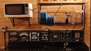 A kitchen with a microwave, a sink, and a coffee machine. There are various kitchen utensils and a shelf with decorative items.
