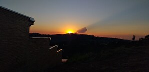 A sunset over a hilly landscape with a brick building in the foreground. - La Villa Chalés (SP)