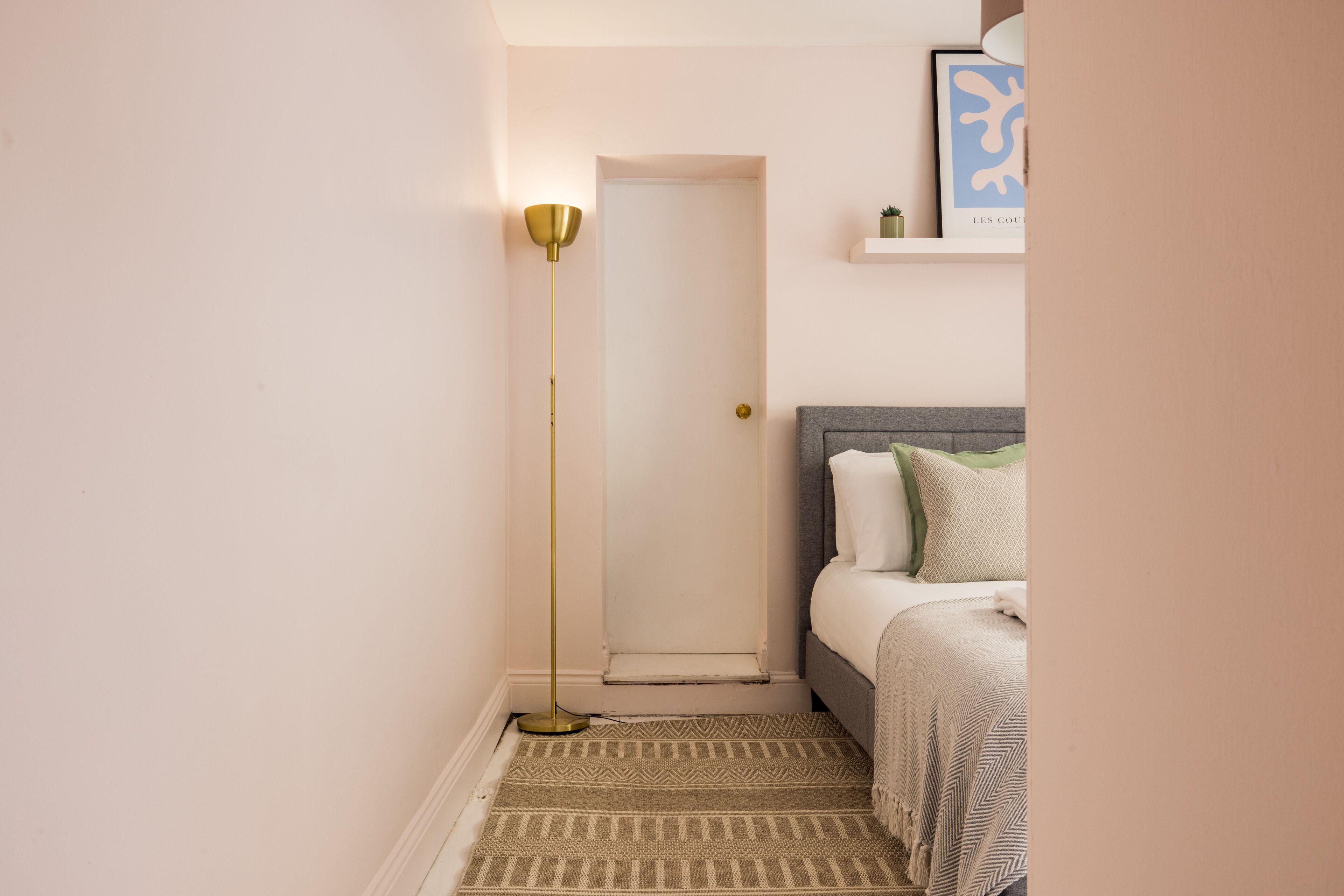 A bedroom with a bed, a floor lamp, a rug, and a door.