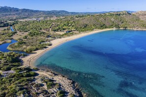 Vista aérea de una zona costera con mar azul cristalino, playa arenosa y vegetación circundante.