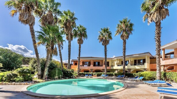 A pool area with palm trees, lounge chairs, and a building with balconies. - Studio apartment 2 beds, about 30 square meters, living room with kitchenette and single beds that can be joined together, bathroom with shower. Possibility of cot (with supplement). <br>Comfortably furnished apartments, they can be on the ground floor w (Palau)