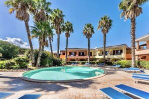 A pool area with palm trees, lounge chairs, and a building with balconies. - Studio apartment 2 beds, about 30 square meters, living room with kitchenette and single beds that can be joined together, bathroom with shower. Possibility of cot (with supplement). <br>Comfortably furnished apartments, they can be on the ground floor w (Palau)