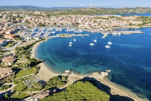 An aerial view of a coastal town with a marina, clear blue waters, and a mix of residential and commercial buildings.