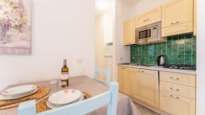 A compact kitchen with a microwave, stove, and green-tiled backsplash. There is a dining table with plates and a bottle of wine. - Studio apartment 2 beds, about 30 square meters, living room with kitchenette and single beds that can be joined together, bathroom with shower. Possibility of cot (with supplement). <br>Comfortably furnished apartments, they can be on the ground floor w (Palau)