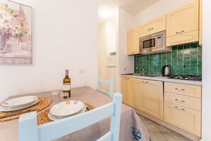 Una cocina funcional con microondas, estufa y salpicadero de azulejos verdes. Se aprecia una mesa con platos y una botella de vino.