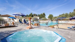 Ein Poolbereich mit Liegestühlen und Sonnenschirmen, umgeben von Kübelpflanzen und einem Holzzaun.
