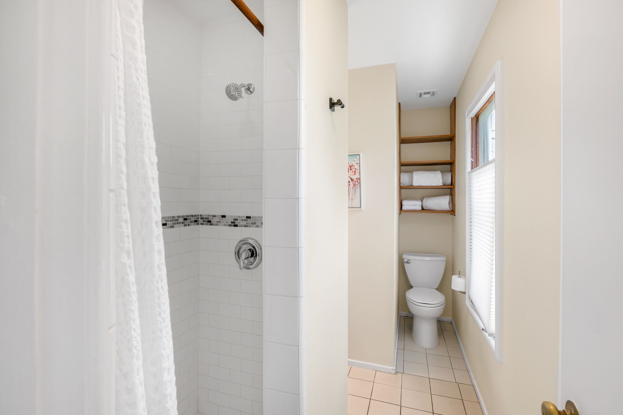Une salle de bain avec une douche, des toilettes et des étagères où sont rangées les serviettes.