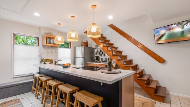 Eine moderne Küche mit einer zentralen Kochinsel, Holzbarhocker, Pendelleuchten, einem eingebauten Herd und einer Holztreppe.