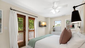 Ein Schlafzimmer mit Bett, Deckenventilator, Fenster mit Blick und einer zur Außenwelt führenden Tür.
